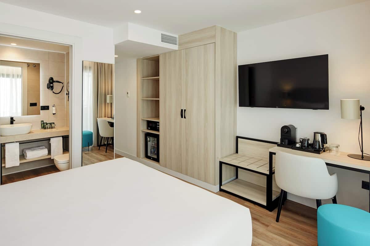 Una habitación de hotel moderna con una cama grande, un escritorio con una silla, un televisor y un armario.