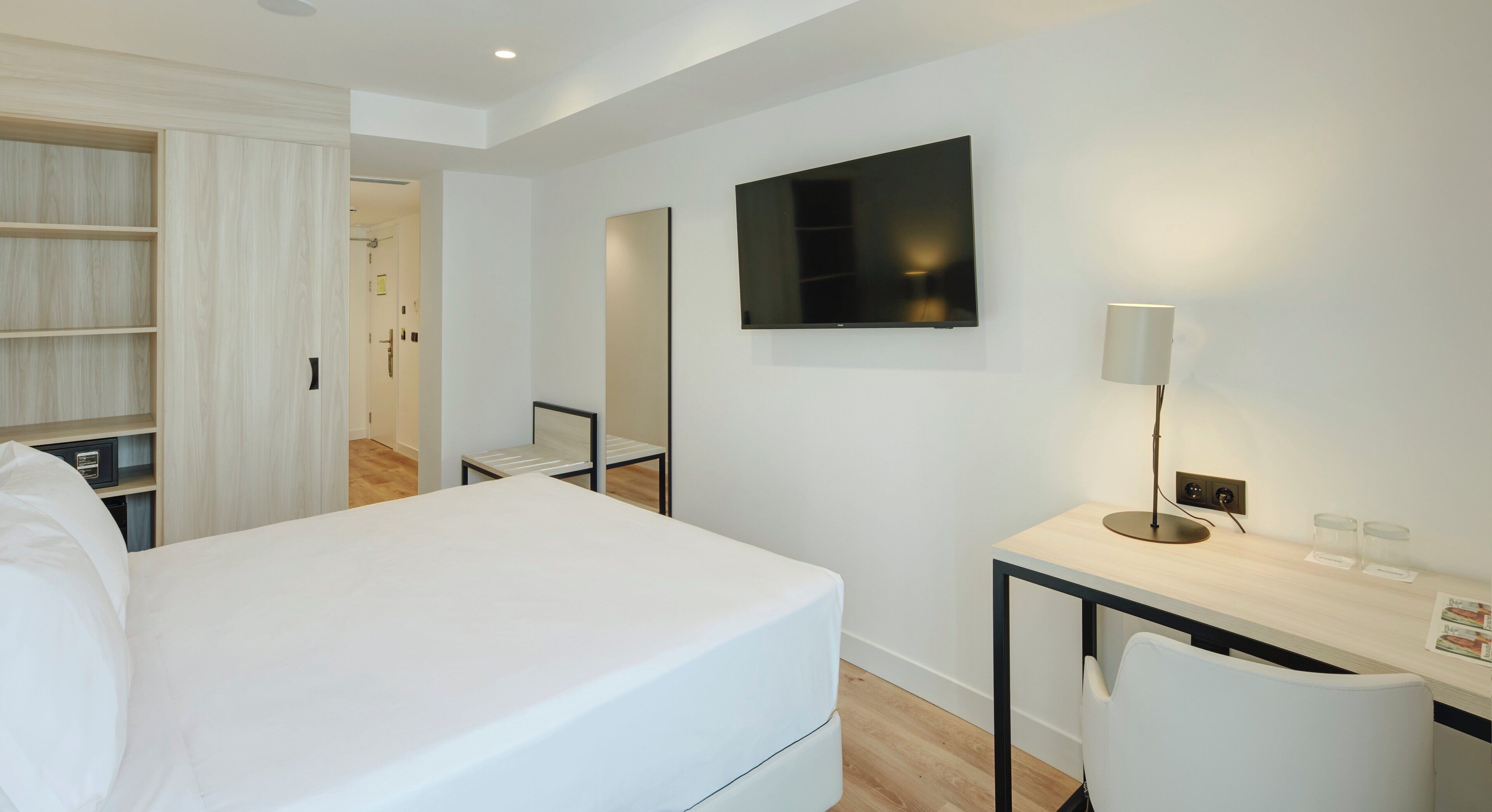 Una habitación de hotel con cama, escritorio, silla, televisión y lámpara.