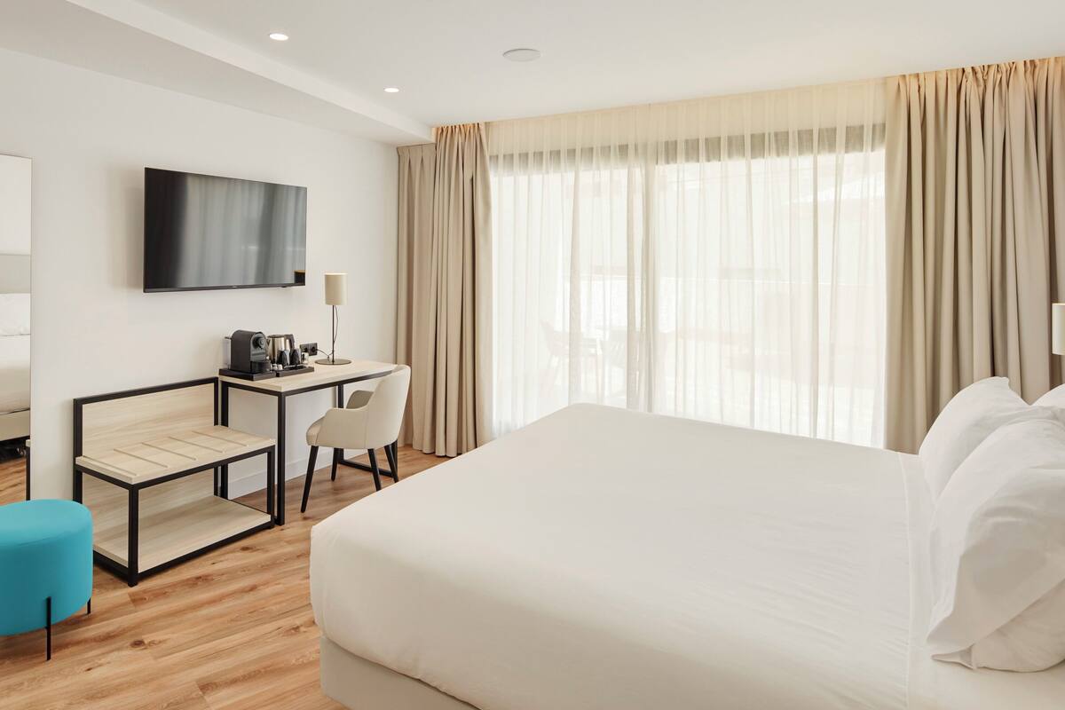 A hotel room with a large bed, a desk with a chair, a television, and a window with curtains.