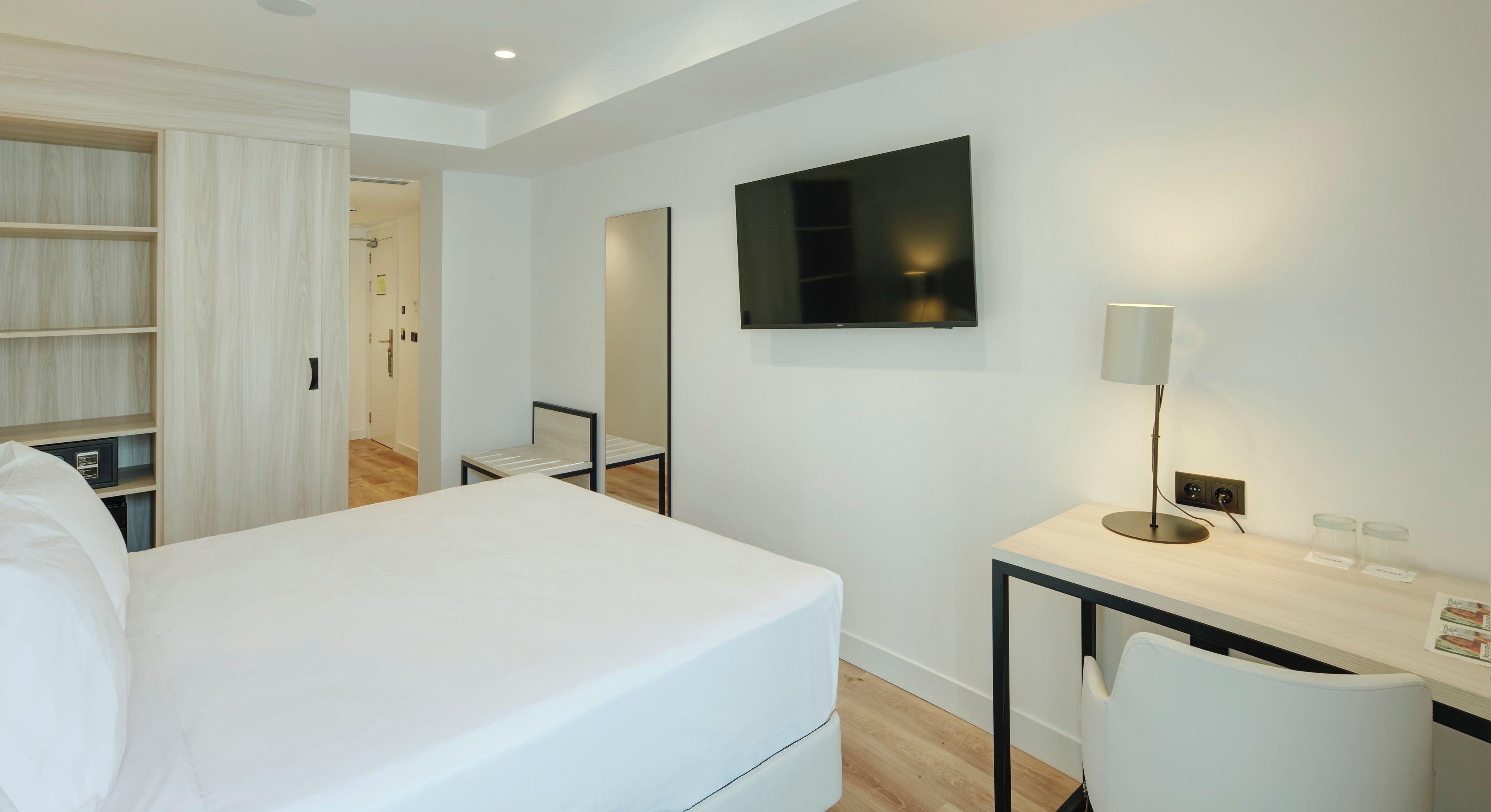 Une chambre d’hôtel avec un lit, un bureau avec une lampe, une télévision et une armoire.