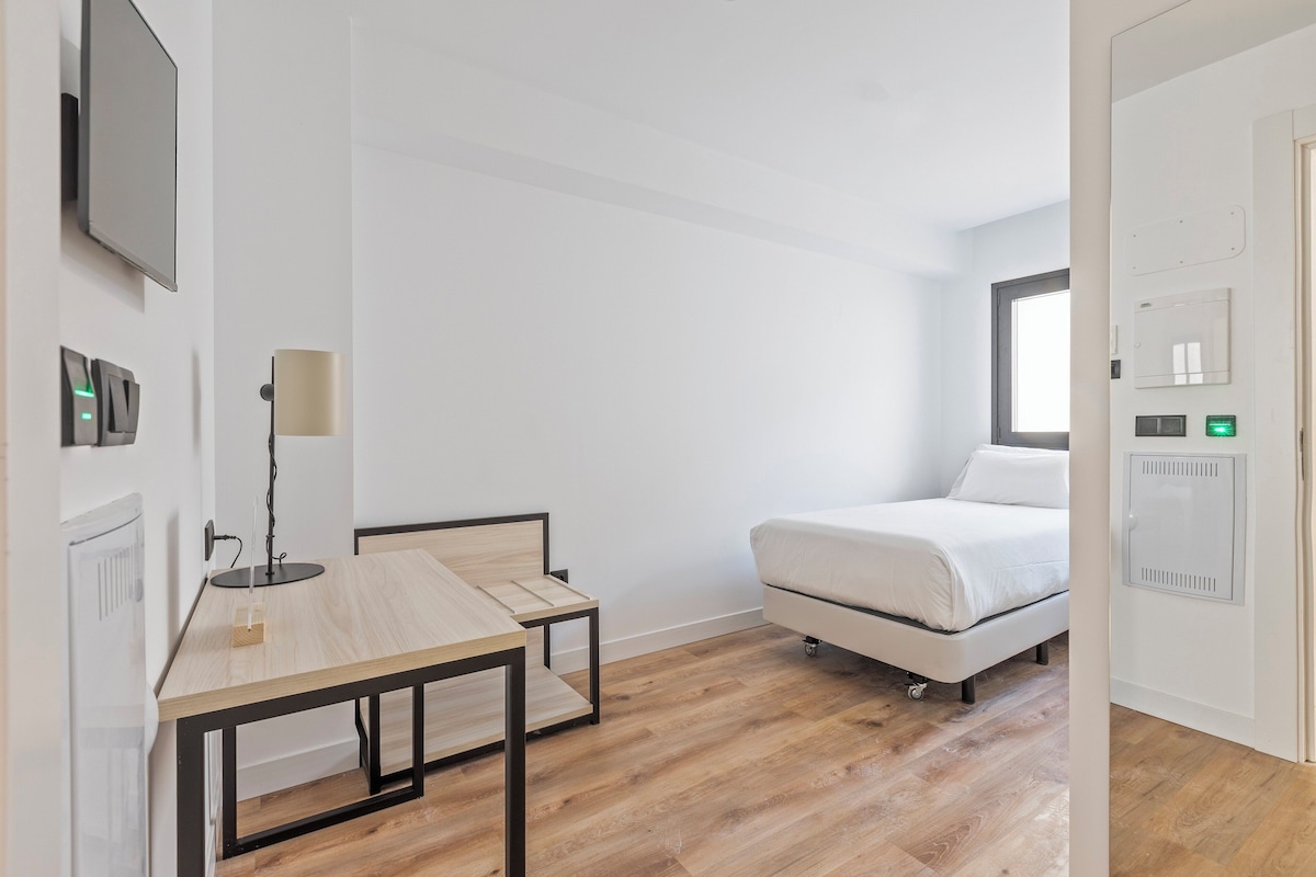 Une chambre à coucher moderne et minimaliste, avec un lit, une petite table et un bureau.