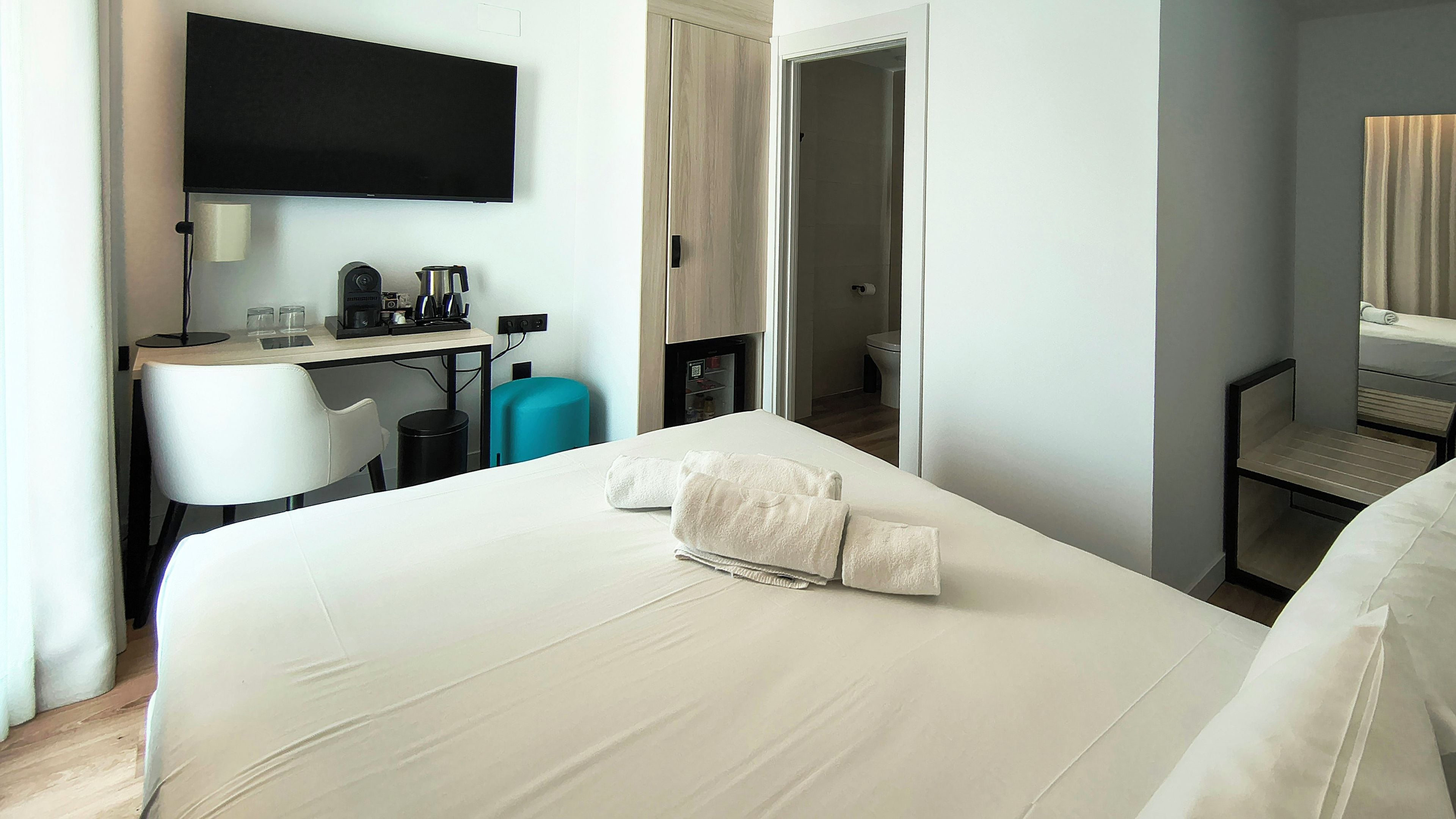 Habitación de hotel con cama, escritorio con computadora, televisor y baño visible a través de una puerta abierta.