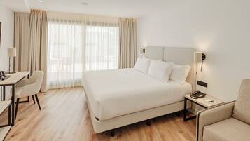 Una habitación de hotel con una cama grande, un escritorio, una silla y una mesita de noche con lámpara.