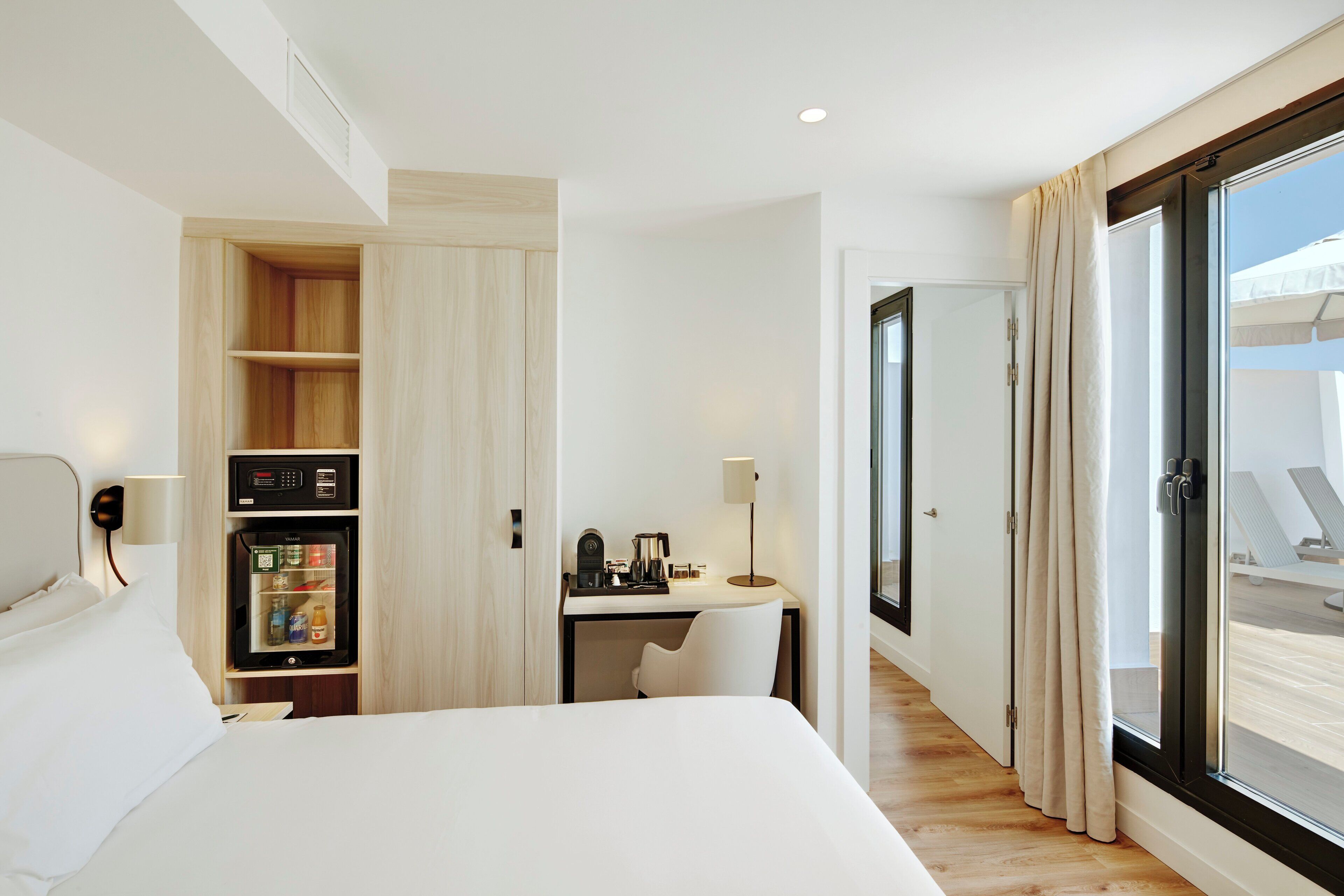 Hotelkamer met een bed, een bureau met stoel, een minibar en een schuifdeur naar het balkon.