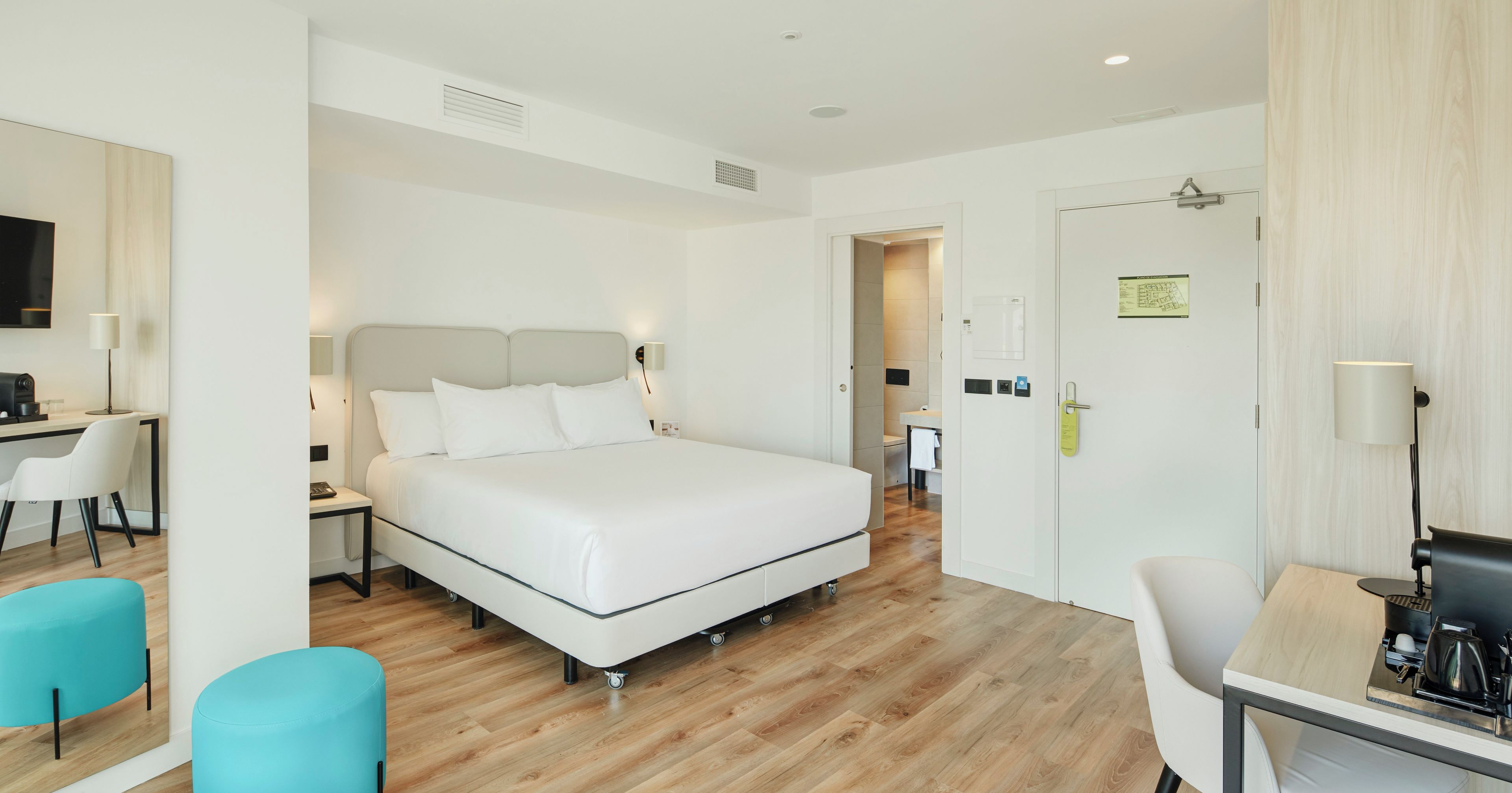 A hotel room with a bed, a desk, a chair, and a coffee machine.