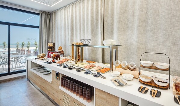 A buffet setup with various food items, utensils, and glassware. - Sercotel Cruz del Mar  (Chipiona)