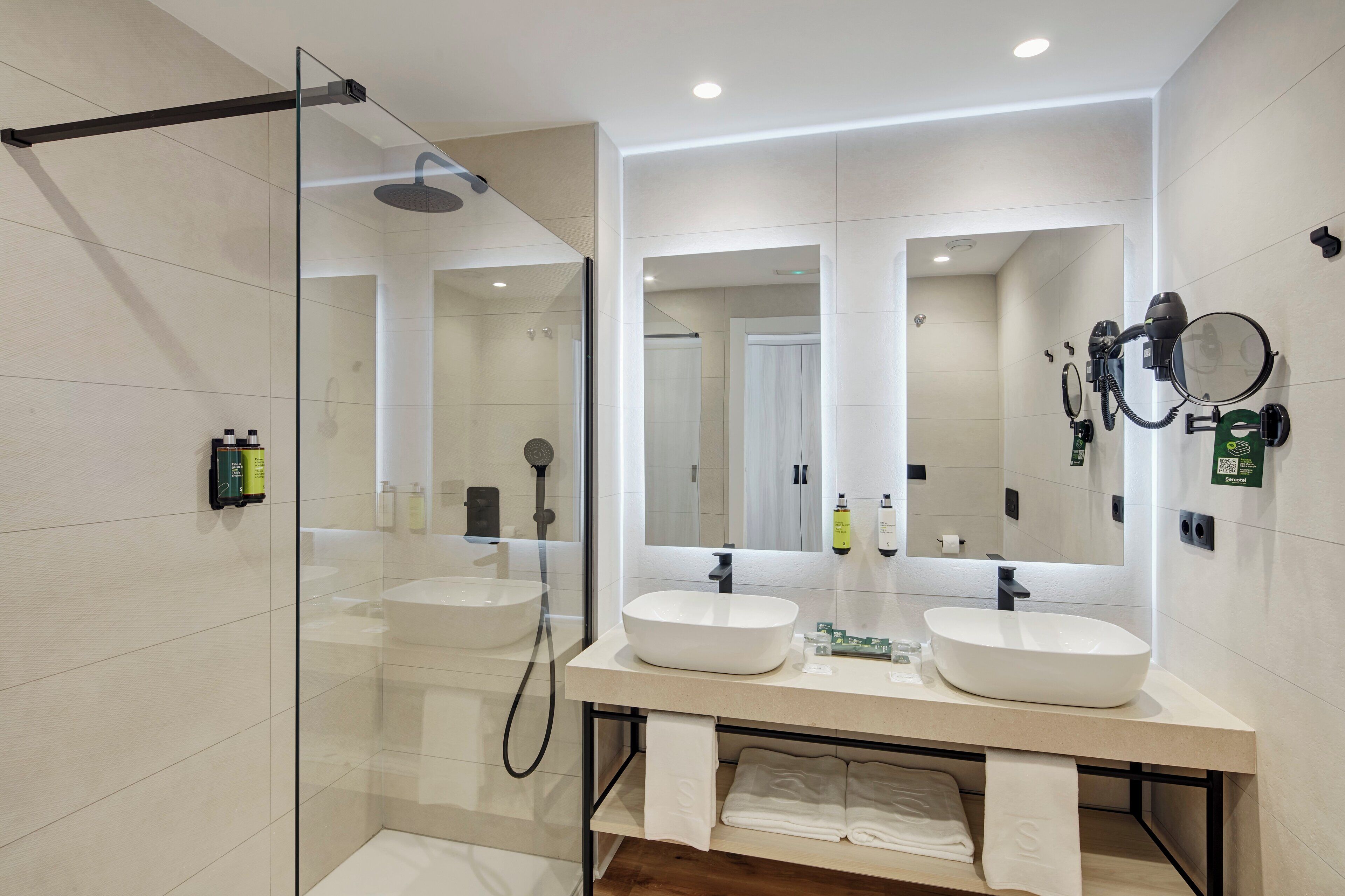 A modern bathroom with two sinks, a glass shower enclosure, and a large mirror.