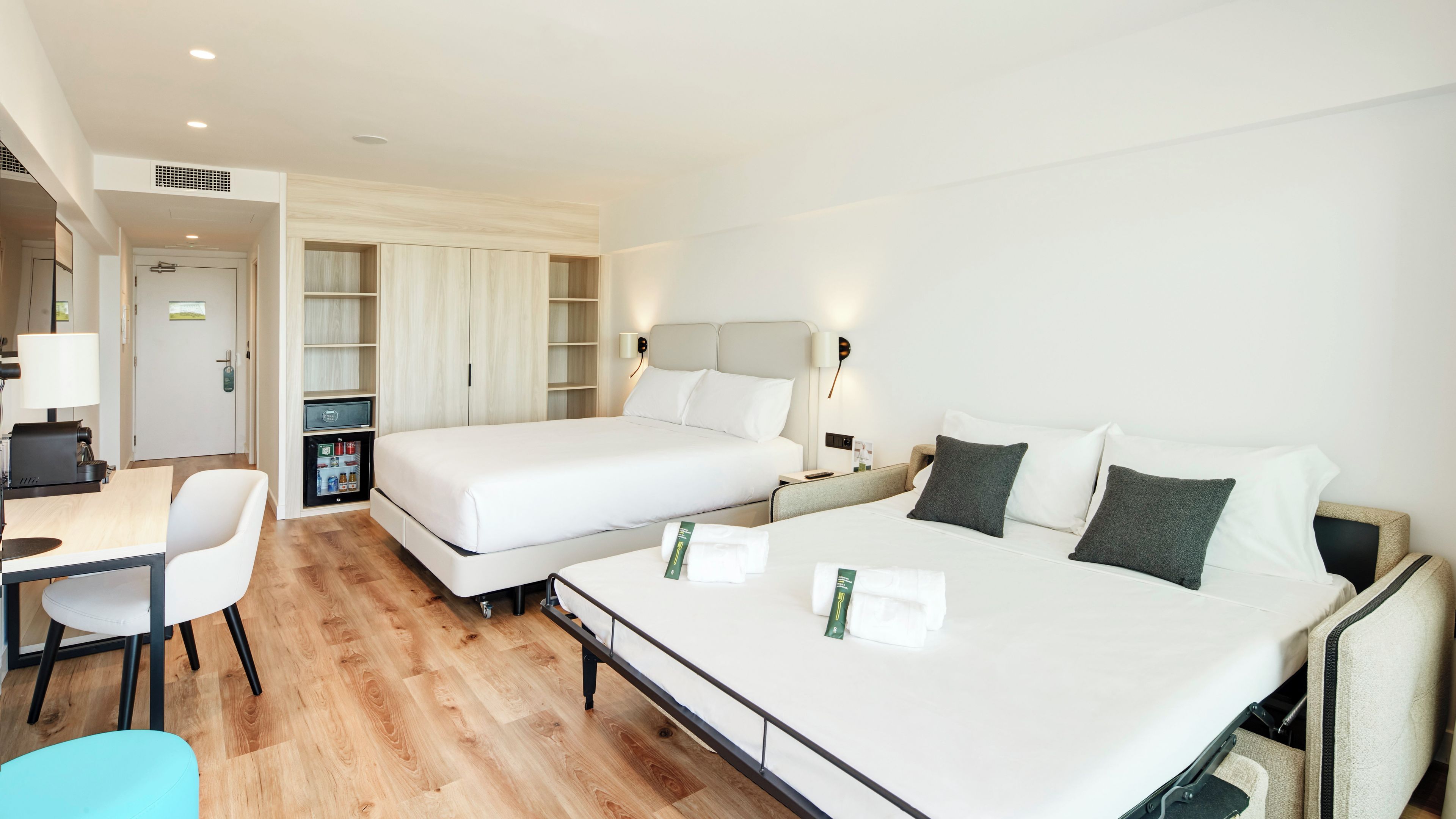 Una habitación de hotel con una cama grande, un escritorio, una silla y un minibar.