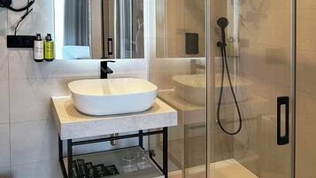 Un baño moderno con ducha envuelta en vidrio, lavamanos con espejo y secador de pelo montado en la pared.