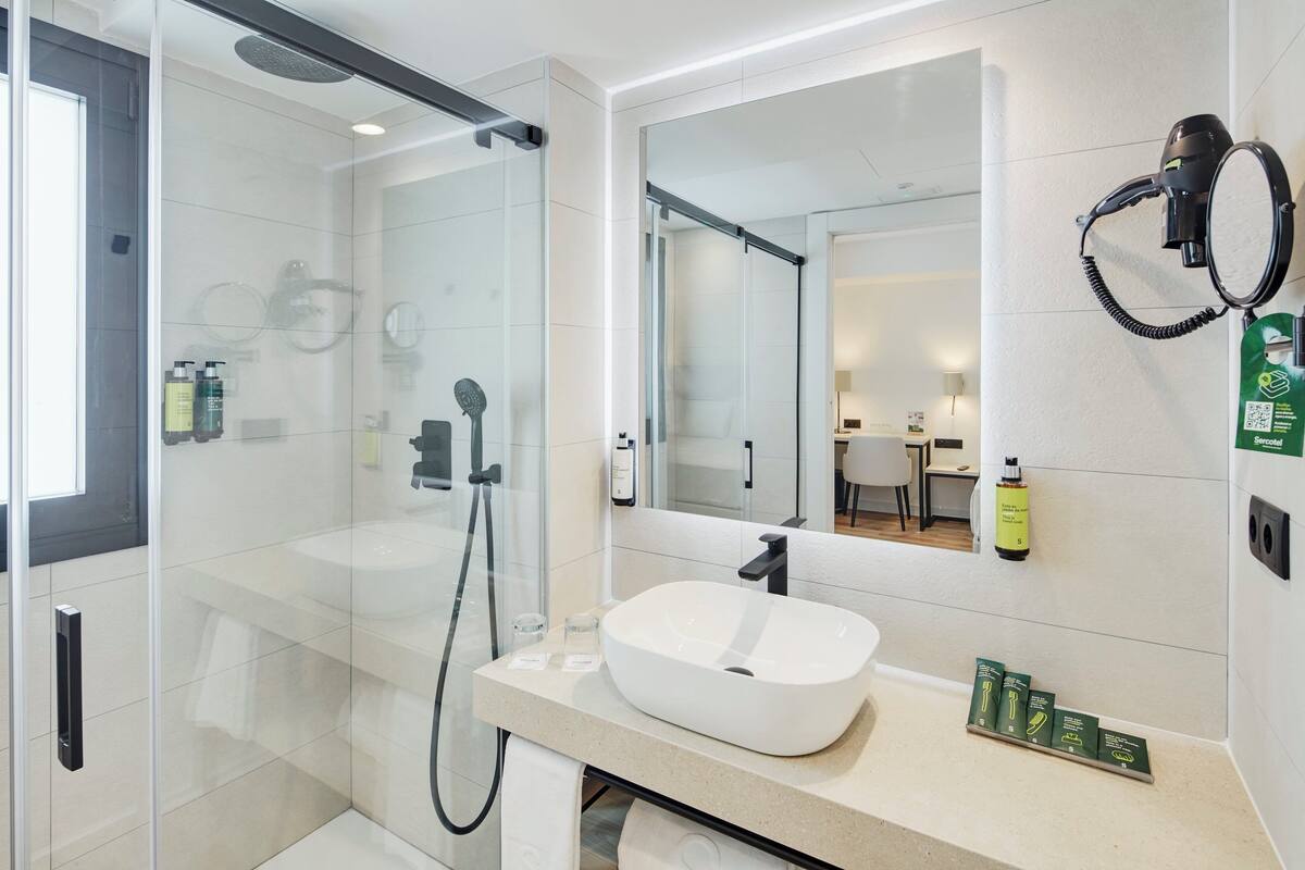 A modern bathroom with a glass-enclosed shower, a white sink, and a large mirror.