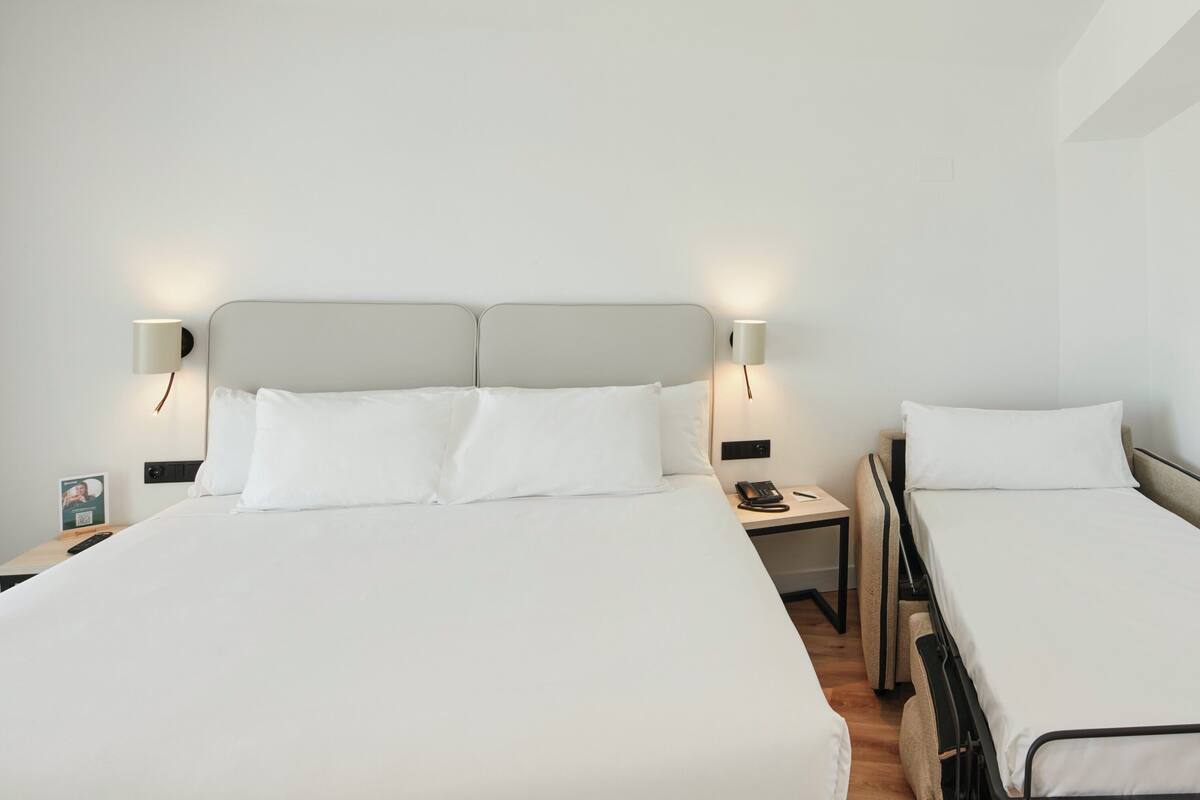 A hotel room with two beds, each with white linens and headboards. There are bedside tables with lamps and a phone.