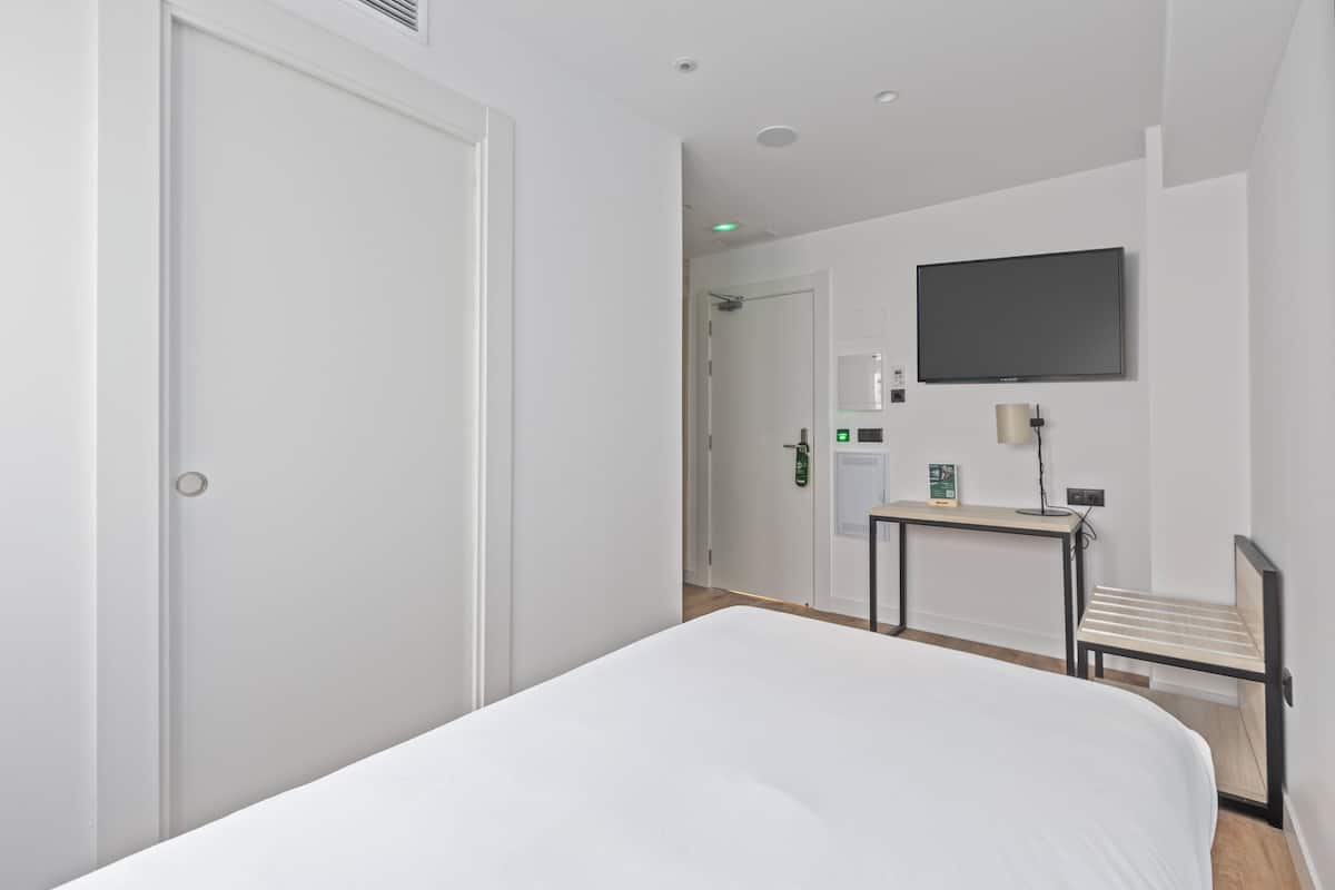 Una habitación de hotel con una cama, un escritorio, una silla, un televisor y una puerta.