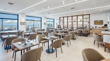 A modern restaurant with multiple tables and chairs, large windows offering a view of the city, and a variety of decorative items on shelves.