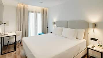 A hotel room with a large bed, a desk, a chair, a nightstand, and a window with curtains.
