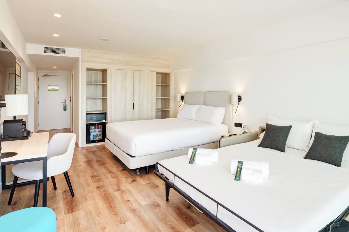 A hotel room with two beds, a desk, a chair, and a minibar.