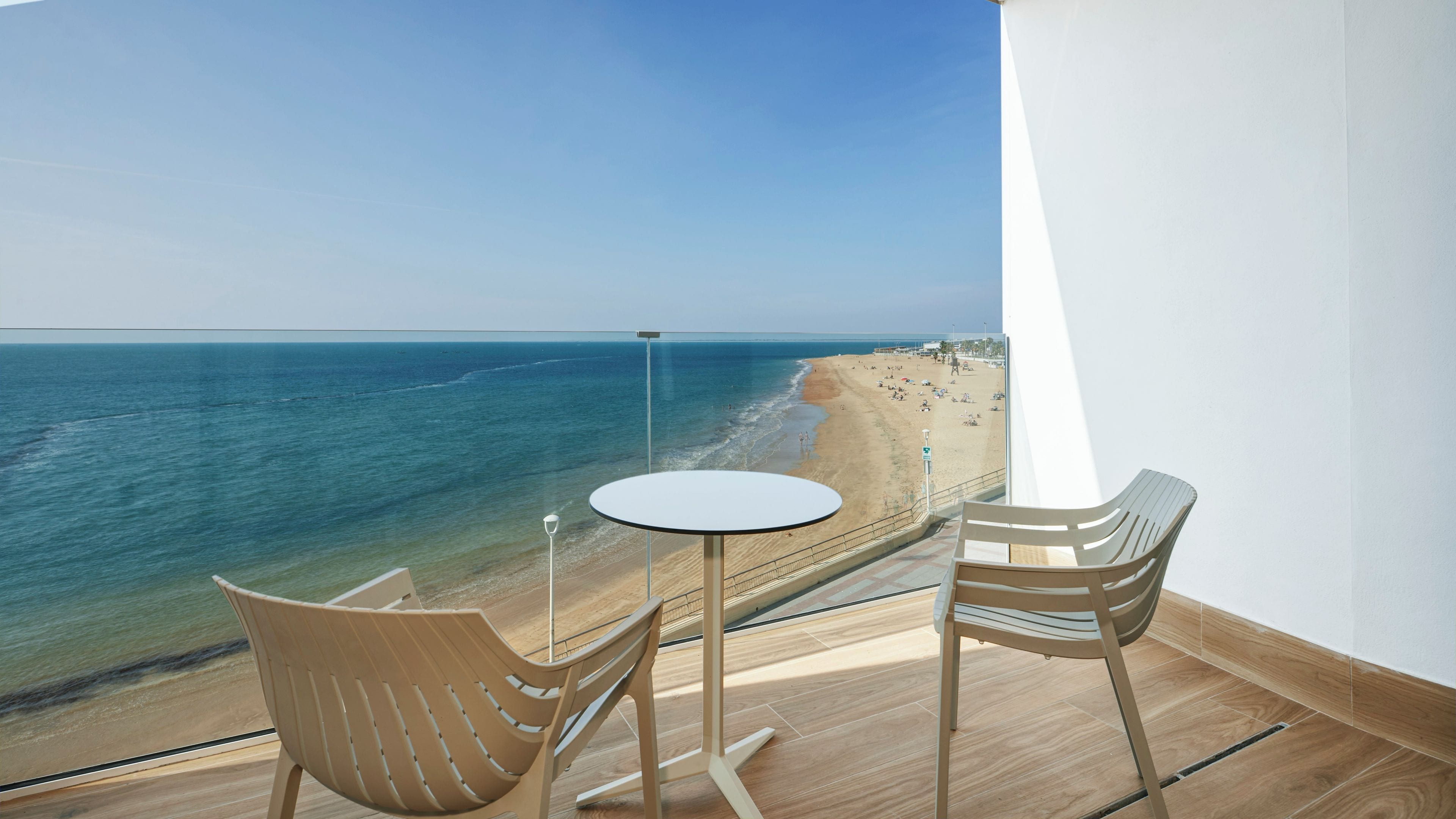 A balcony with a view of the beach, a round table, and two chairs.