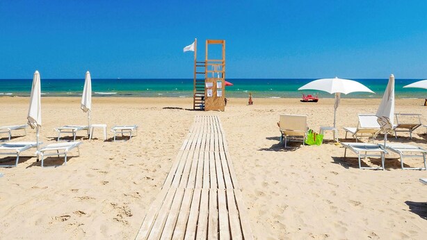 A beach with a wooden walkway leading to a lifeguard tower, white beach umbrellas, and sun loungers. - Beautiful home in Marina di Modica (Marina di Modica)