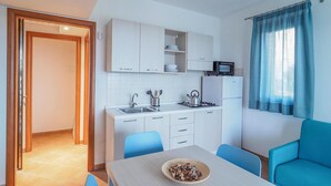 A compact kitchen with white cabinets, a stove, sink, and a microwave. There is a dining table with chairs and a bowl of mushrooms. - Beautiful home in Marina di Modica (Marina di Modica)