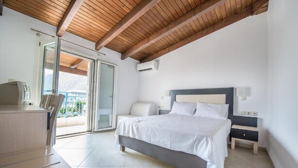 A modern bedroom with a bed, bedside tables, a desk, and a sliding glass door leading to a balcony. - DELLIS (Kamena Vourla)