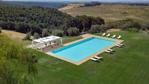 Vista aérea de una piscina con sombrilla, rodeada de césped y árboles.