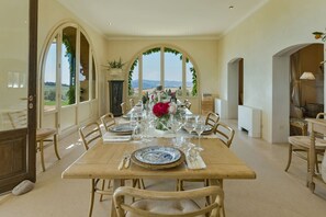 A dining room with a long table set for a meal, large windows with a view, and a decorative vase with flowers.