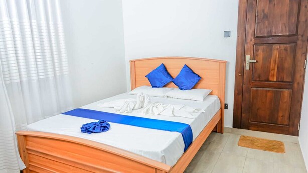 Una cama individual con estructura de madera, ropa de cama blanca y detalles en azul.
