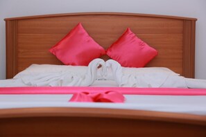 Een keurig opgemaakt bed met witte lakens en twee rode kussens, een houten hoofdbord en een roze lint op het bed.