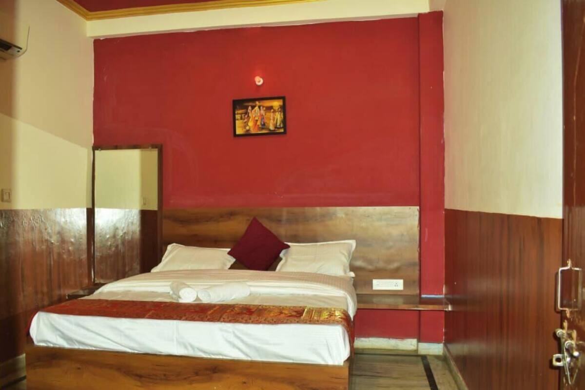 A room with a large bed, wooden headboard, red walls, and a small painting above the bed.