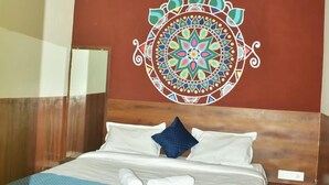 A hotel room with a bed, a ceiling fan, and a decorative wall hanging. - Rudra Hotel (Varanasi)