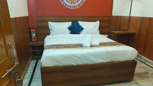A neatly made bed with white linens and a blue pillow, a wooden headboard, and a patterned wall decoration. - Rudra Hotel (Varanasi)