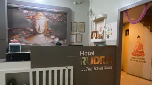 A hotel reception area with a modern design, including a reception desk, a large flat-screen TV, and a decorative Buddha statue. - Rudra Hotel (Varanasi)