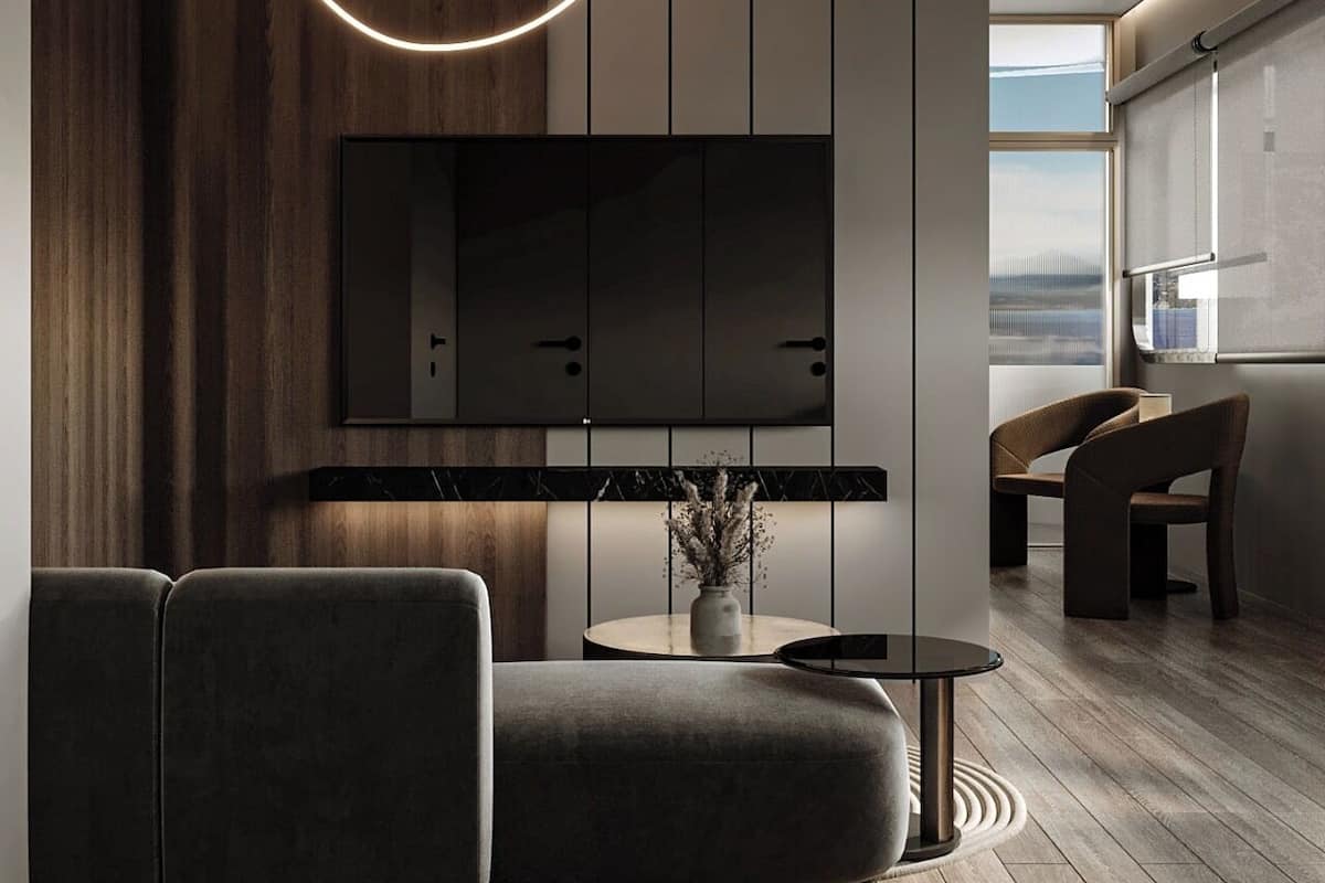 A modern living room with a sectional sofa, a round coffee table, and a flat-screen TV mounted on the wall.