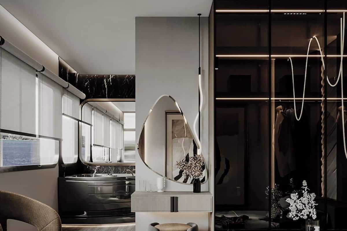 A modern bedroom with a large bed, a small seating area, a kitchen in the background, and a unique curved mirror.