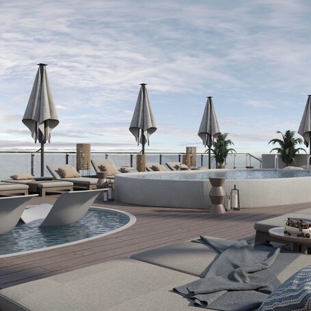 A rooftop pool area with lounge chairs, umbrellas, and a hot tub.
