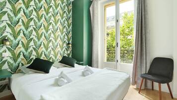 A hotel room with a bed, a chair, a window with curtains, and a green wall with a leaf pattern.