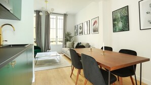 Eine moderne Küche mit integriertem Backofen, ein Essbereich mit Holztisch und schwarzen Stühlen sowie eine Wohnbereich mit Sofa und Pflanze.