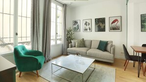 Ein modernes Wohnzimmer mit einer Couch, einem grünen Sessel, einem Esstisch und Kunstwerken an der Wand.