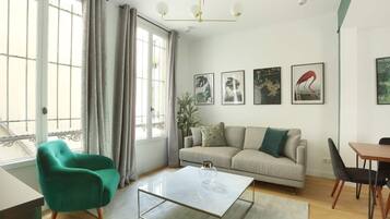 A modern living room with a sofa, a green armchair, a dining table, and artwork on the wall.