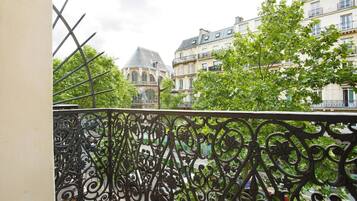 A balcony with ornate wrought iron railings overlooking a street with historic buildings and lush greenery.