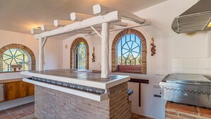 A kitchen with a central island, brick walls, arched windows, and a built-in grill. - Awesome home in Guaro (Guaro)
