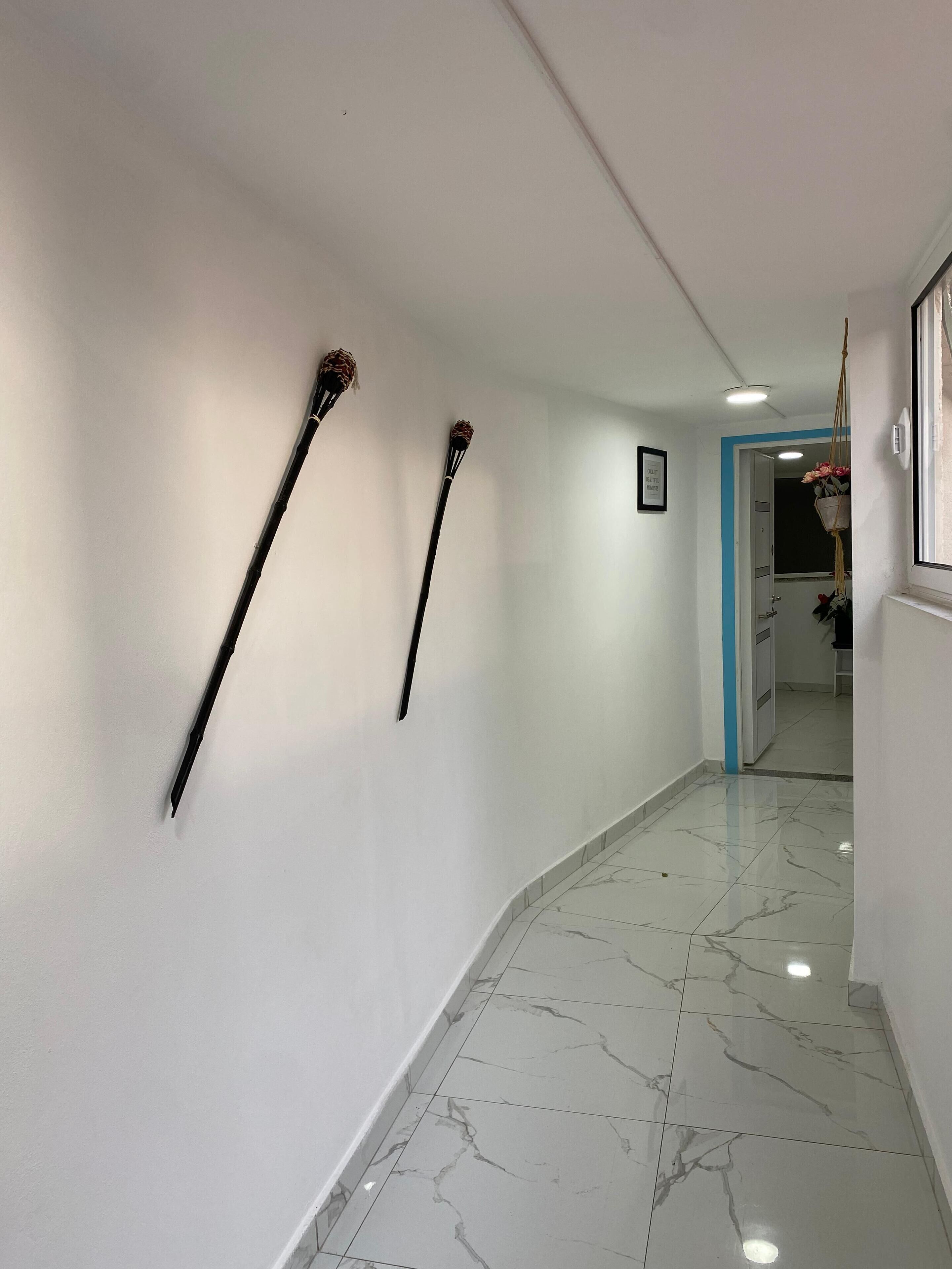 Un pasillo con paredes blancas y piso de mármol. Se observan dos objetos negros montados en la pared.