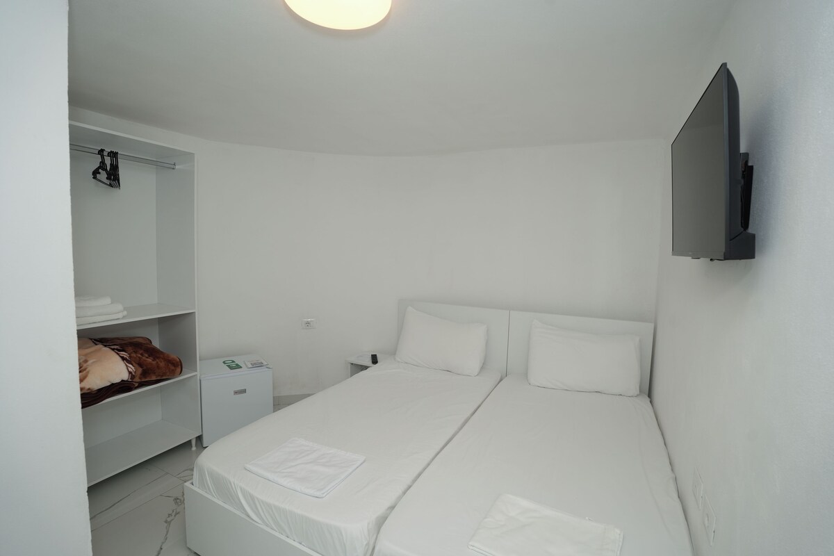 A minimalist bedroom with a single bed, a wardrobe, a bedside table, and a wall-mounted TV.