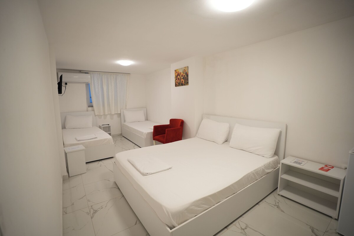 A modern hotel room with a large bed, a small desk, a chair, and a window with curtains.