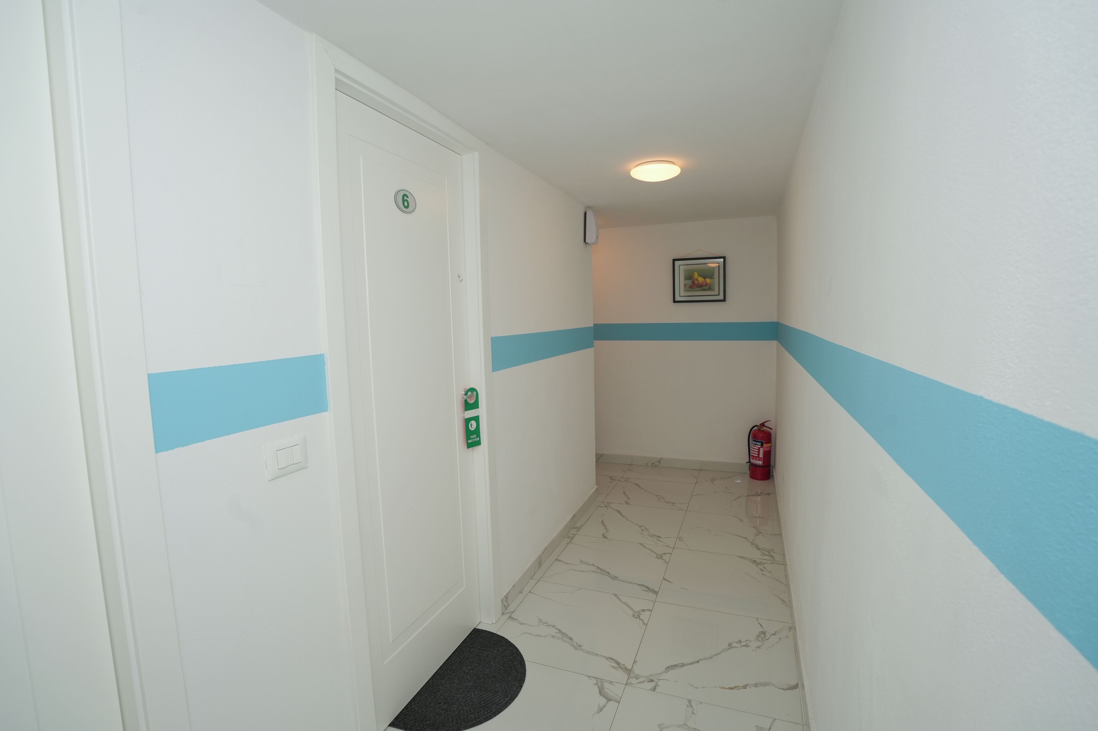 A hallway with a white door marked with the number 6, a fire extinguisher, and a small mat at the entrance.