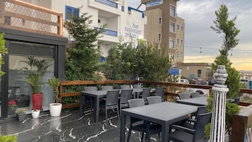 Relax in the outdoor seating area with tables and chairs, surrounded by lush greenery and a view of the surrounding buildings.
