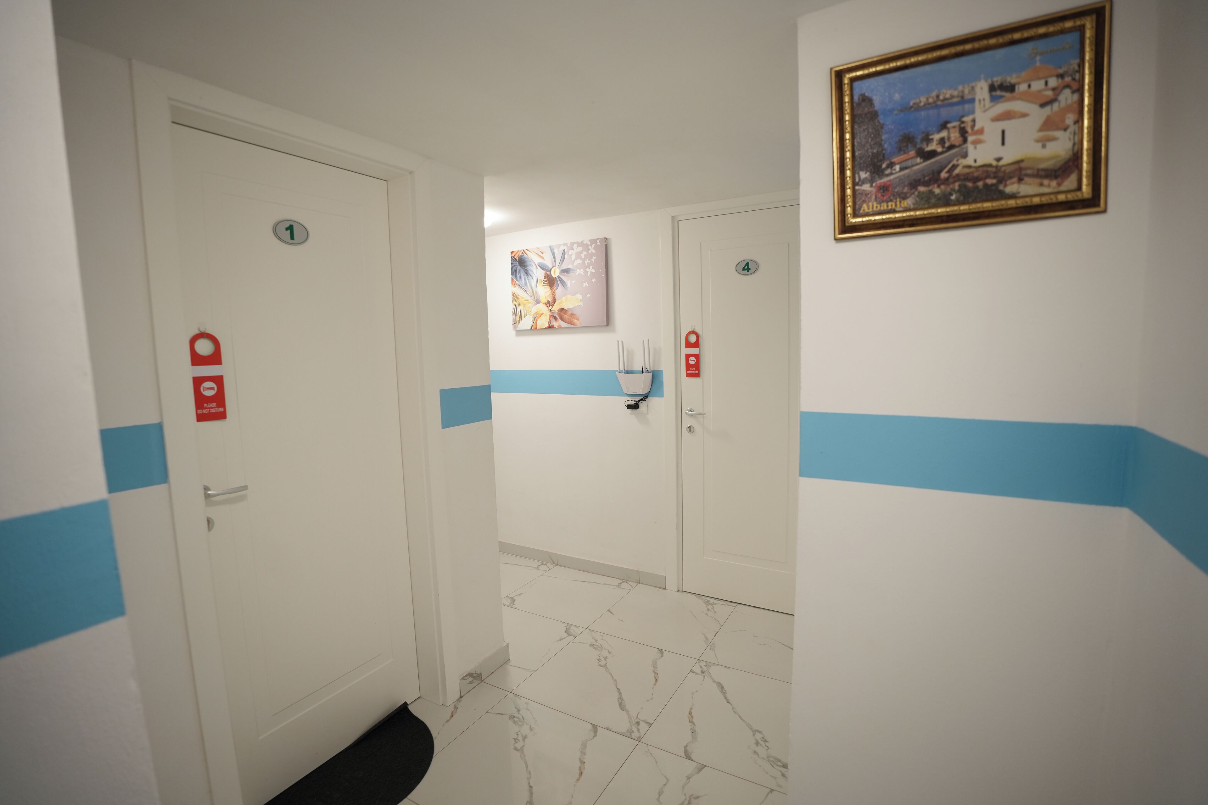 Un pasillo con puertas numeradas 1 y 4, un cuadro en la pared y una franja azul en las paredes.