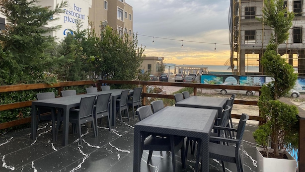 An outdoor seating area with tables and chairs, surrounded by greenery and overlooking a cityscape with buildings and a construction site. - Enles Hotel (Durrës)