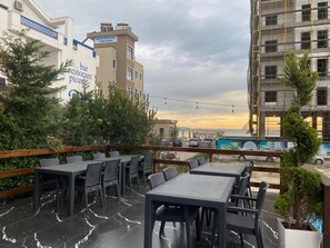 Un espacio al aire libre con mesas y sillas, rodeado de follaje y vistas a un paisaje urbano con edificios y una obra en construcción.