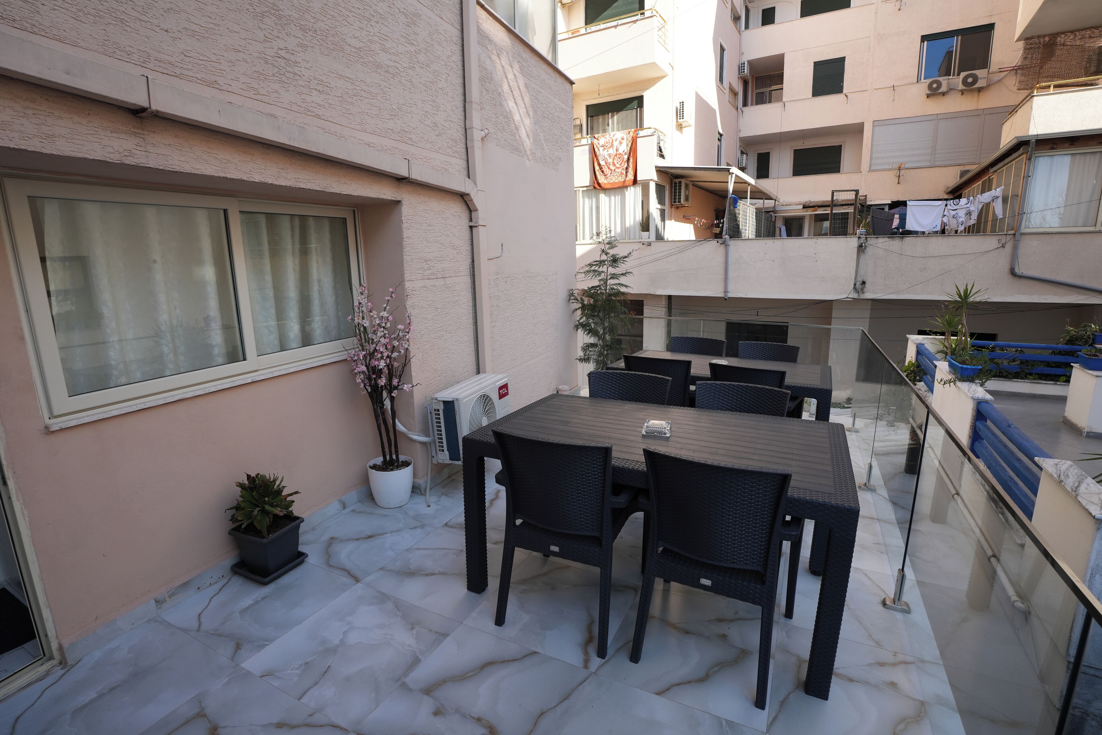 An outdoor patio with a table and chairs, potted plants, and a view of a multi-story building.