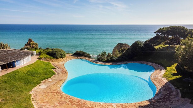 A large, curved swimming pool with a clear view of the ocean in the background. - Prainha Calm Retreat in Alvor (Portimão)